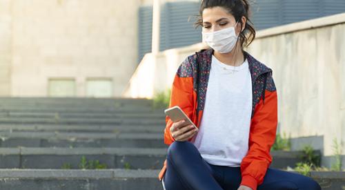 woman sitting on stairs with phone and mask