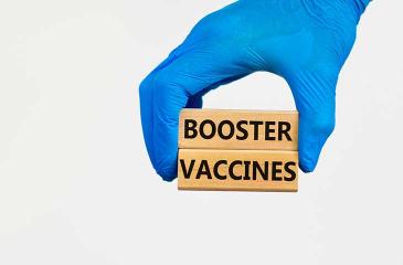 Booster Vaccines wood blocks stacked held by medical gloves
