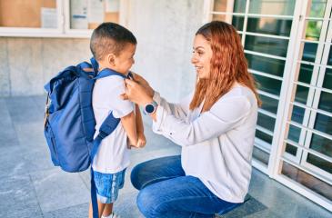 A parent helps a child get their backpack on 
