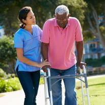 Geriatric Pprson using a walker outside with a health care worker