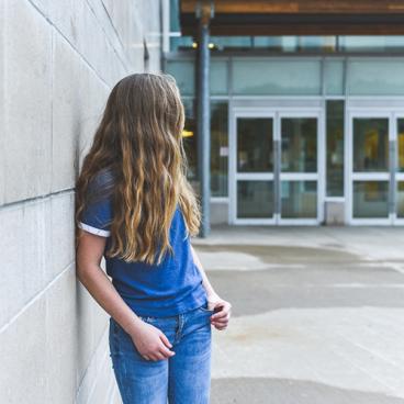 teen girl leaning against wall outside of school